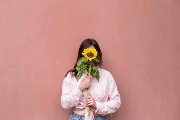 Foto gratuita donna che tiene fiore giallo fresco vicino al viso