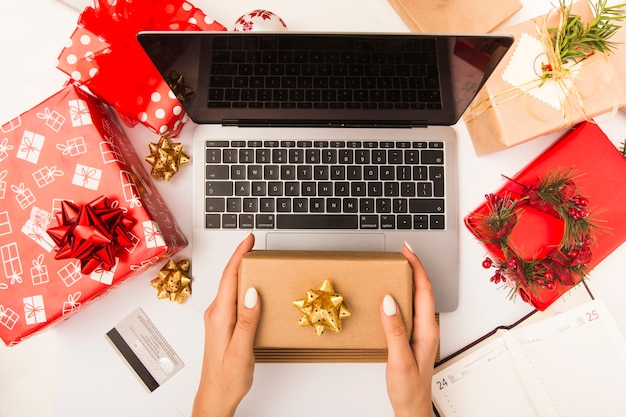 Woman holding gift box while shopping online at table with Christmas decoration