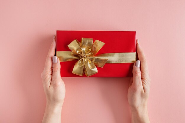 Woman holding giftbox with golden ribbon in hands on pink background