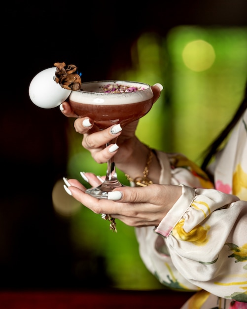 Foto gratuita donna che tiene un bicchiere di cocktail marrone guarnito con petali di fiori secchi