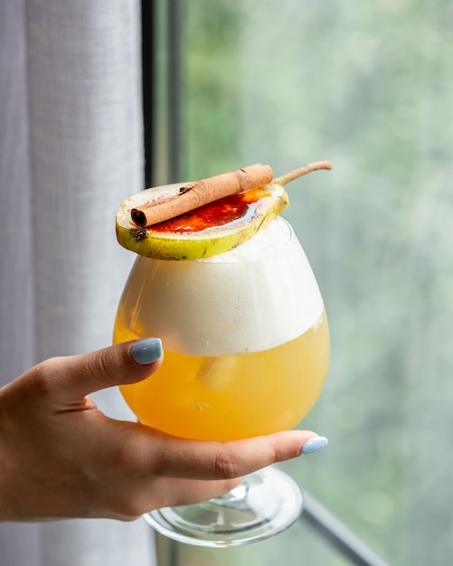 Woman holding a glass of cocktail garnished with pear and cinnamon stick