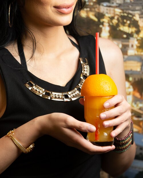 Женщина держит стакан апельсинового сока с половиной апельсина