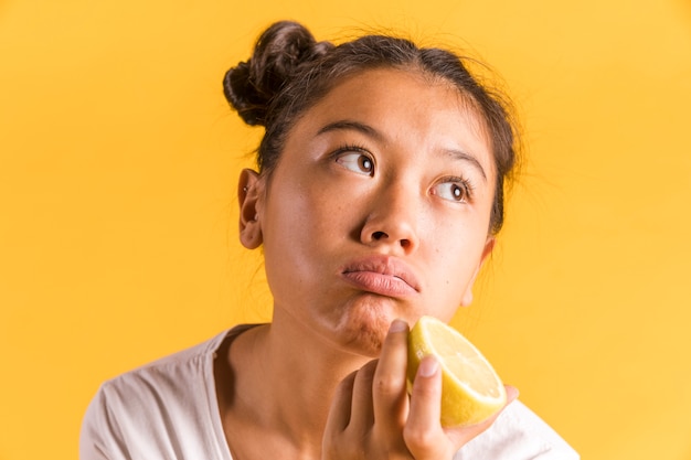 Woman holding half a lemon and looking away