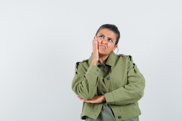 woman holding hand on cheek in jacket, t-shirt and looking pensive.