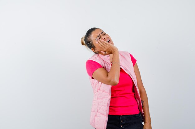 Woman holding hand on cheek in t-shirt, vest and looking mournful 