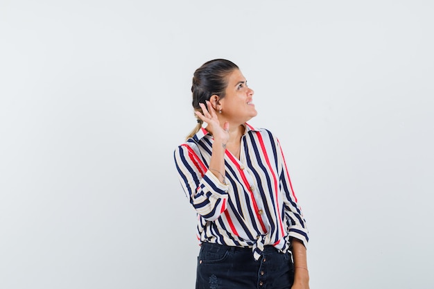 woman holding hand behind ear in shirt, skirt and looking curious