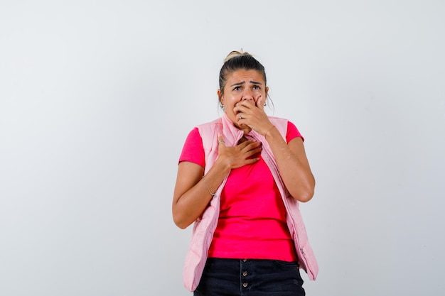 Woman holding hand on mouth in t-shirt, vest and looking wistful