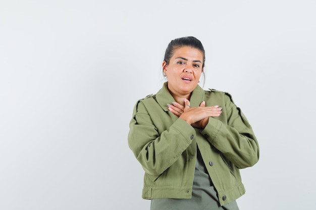 woman holding hands on chest in jacket, t-shirt and looking confident.