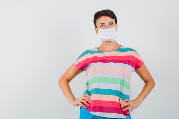 Woman holding hands on waist in striped t-shirt, pants, mask