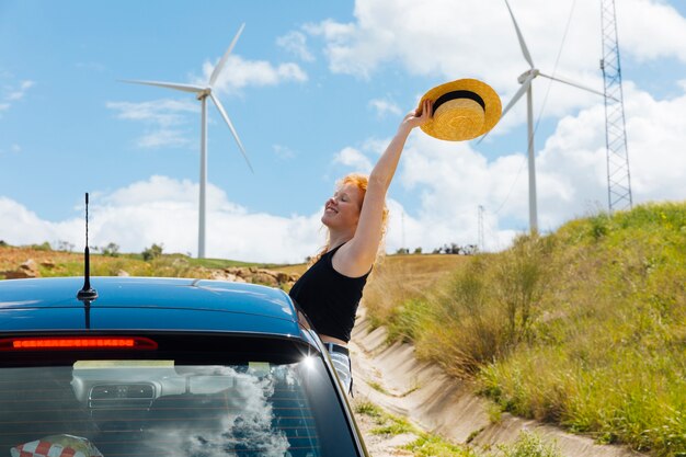 Woman holding hat in arm outstretched out of car window