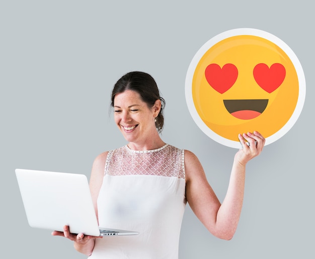 Woman holding a heart eyes emoticon and a laptop