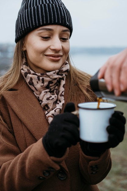 屋外で温かい飲み物を飲むために彼女のカップを保持している女性