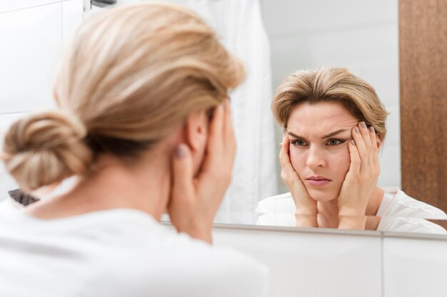 Woman holding her face and looking in the mirror