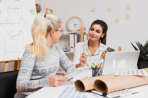 woman holding her glasses and looking at her colleague