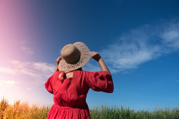 Woman holding her hat while looking up at the sky