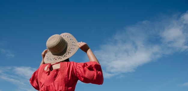 Woman holding her hat while looking up at the sky