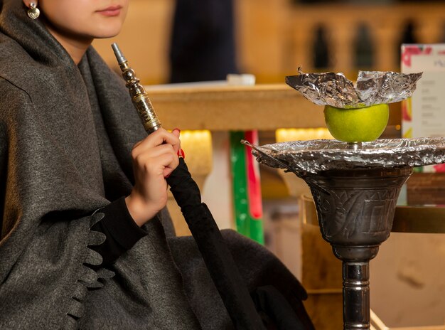 Woman holding hookah pipe sitting at the shisha lounge