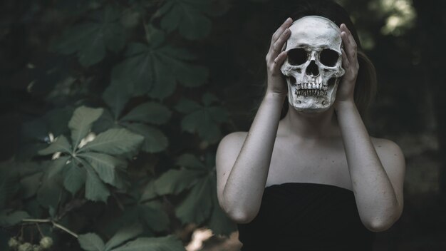 Woman holding human skull in woods daytime