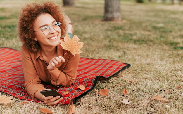 Woman holding a leaf and her phone while staying on a blanket