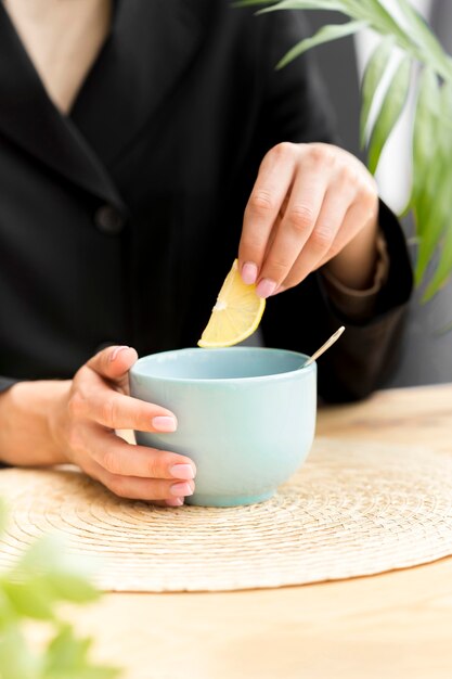 Woman holding lemon slice over cup