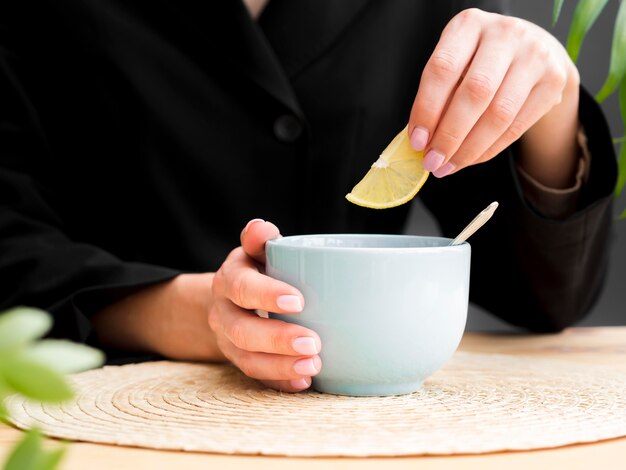 Woman holding lemon slice over teacup