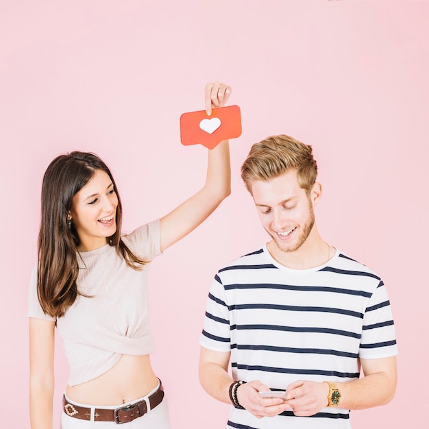 Free photo woman holding love icon over her boyfriend's head using cellphone