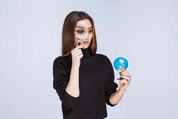 Free photo woman holding a magnifier and checking the world globe.