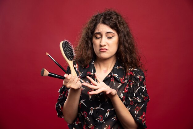 Woman holding makeup brushes and comb.