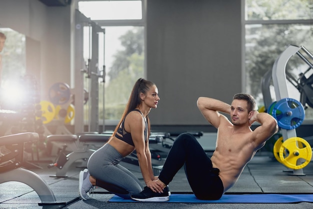 Woman holding man feet down as he doing sit up exercises