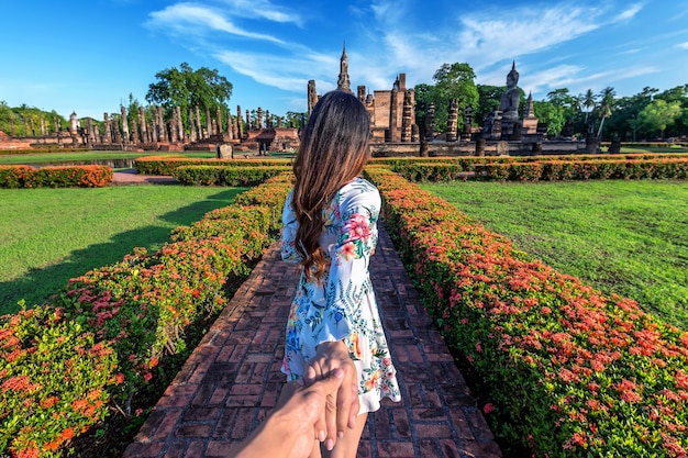 Woman holding man's hand and leading him to Wat Mahathat Temple in the precinct of Sukhothai Historical Park