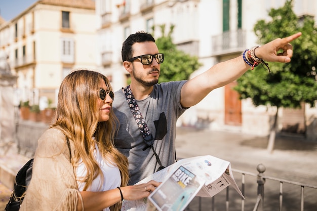 Free photo woman holding map looking at her boyfriend pointing finger