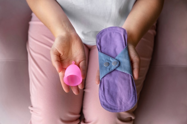 Woman holding menstrual cup and pad high angle