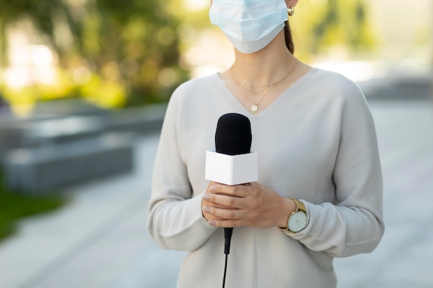 Free photo woman holding a microphone while wearing a medical mask