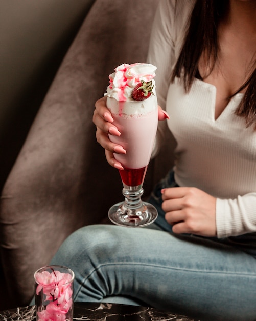 Woman holding a milky cocktail with strawberry syrup and whipping cream.