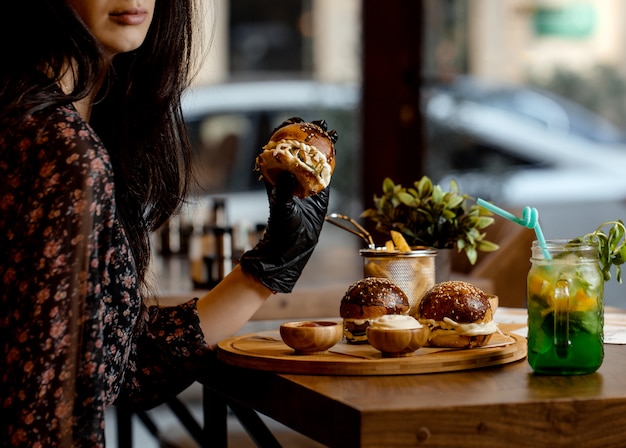 Woman holding mini burger wearing black gloves