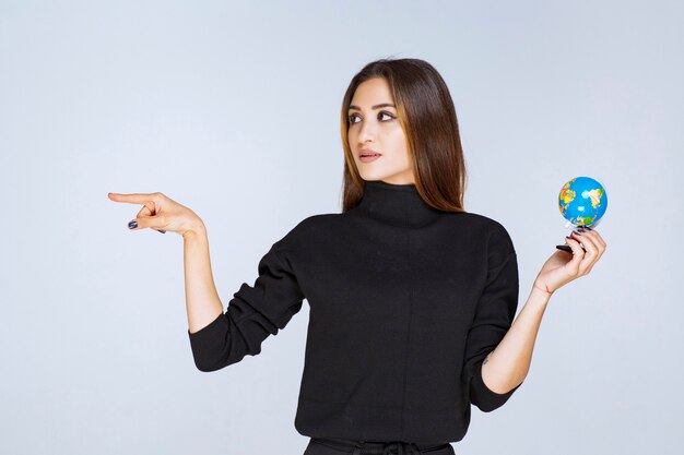 woman holding a mini globe and pointing to somewhere.