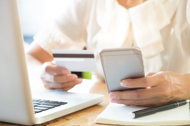 Женщина, держащая мобильный телефон и кредитную карту на ноутбуке для покупок в Интернете