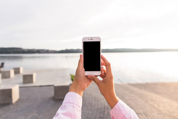 Woman holding mobile phone in front of idyllic lake