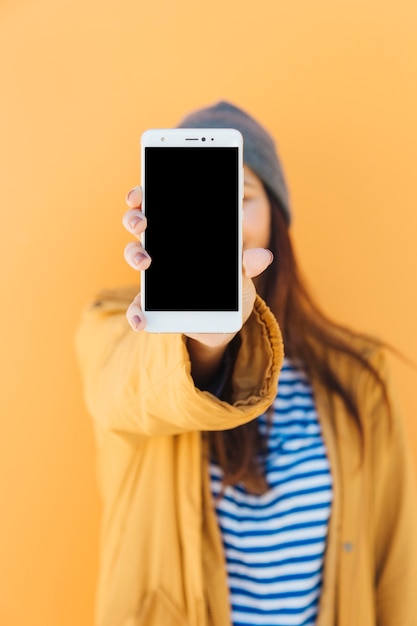 woman holding mobile phone with blank screen standing in front of yellow backdrop