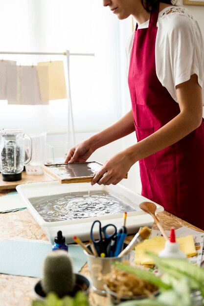 Woman holding mold with pulp over container for making paper