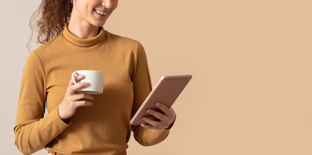 無料写真 朝のコーヒーを保持し、デジタルタブレットを使用している女性