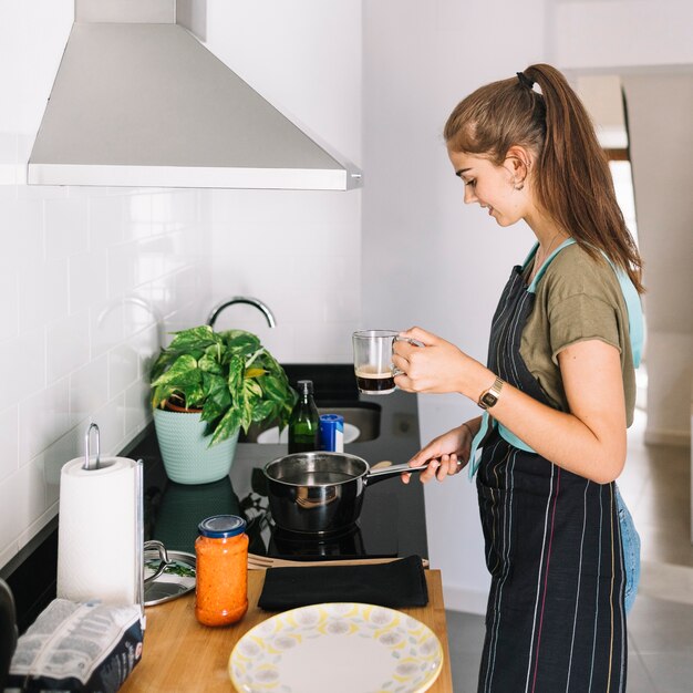 Woman holding mug of coffee preparing food in the kitchen