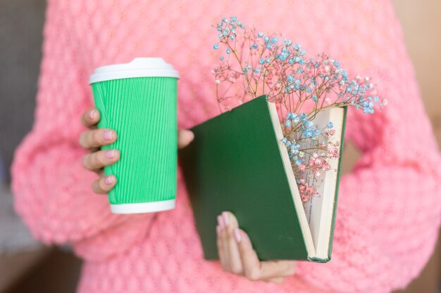 中にドライフラワーの花束とコーヒーの紙コップと開いた本を持っている女性