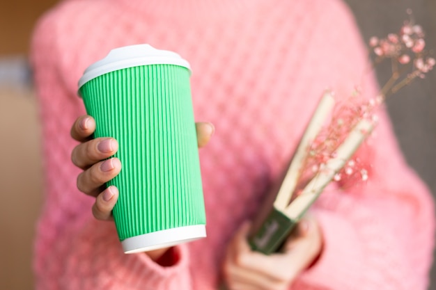 Woman holding an open book with a bouquet of dried flowers inside and a paper cup of coffee 