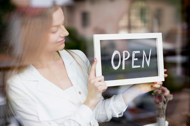 Free photo woman holding open sign in coffee shop window