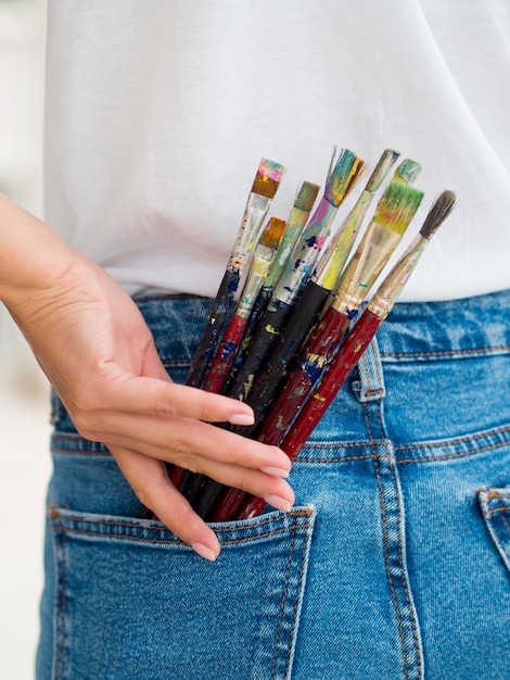 Woman holding paint brushes in back pocket