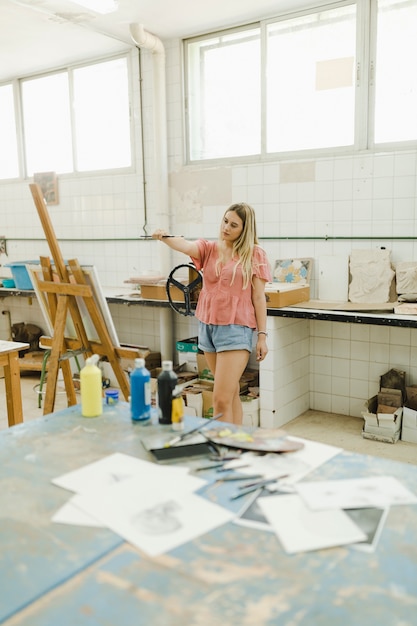 Woman holding paintbrush in front of easel in the workshop