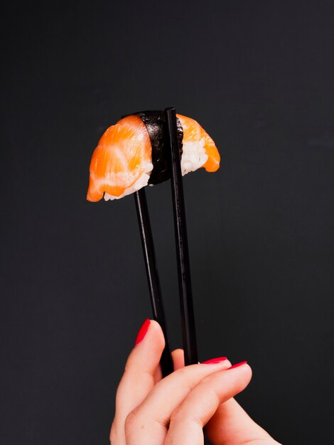 Woman holding a pair of chopsticks with salmon sushi