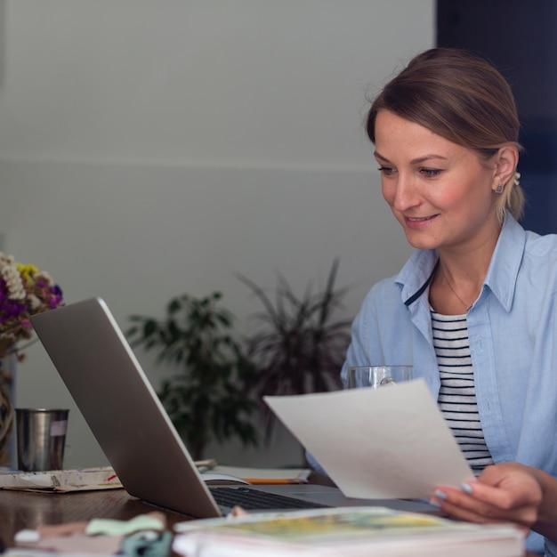 Free photo woman holding paper and looking at laptop