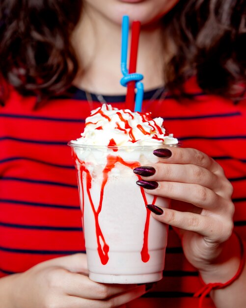 Woman holding a plastic cup of strawberry milkshake with strawberry syrup